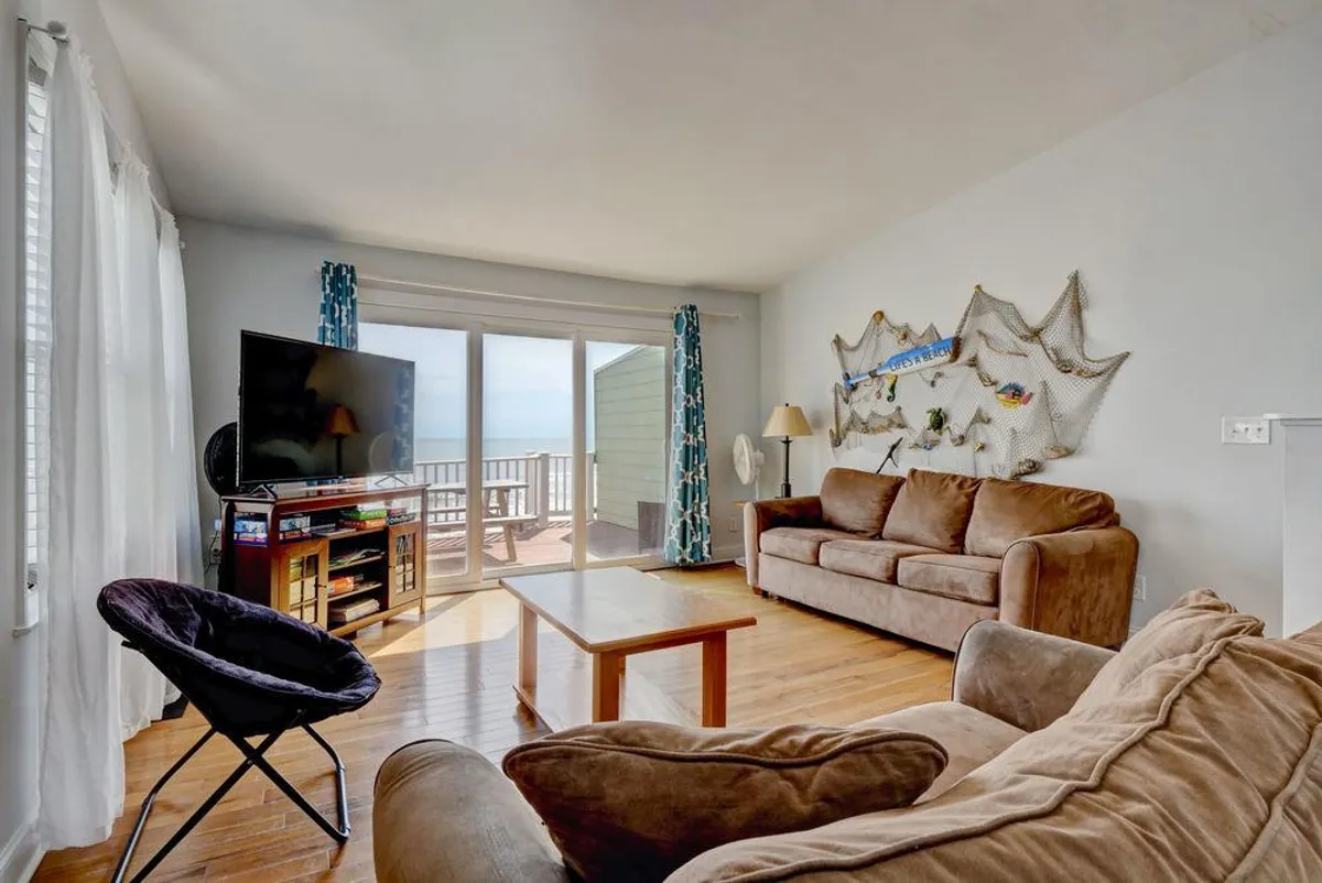 This comfortable living room features large windows framing tranquil ocean views, brown sofas for relaxed seating, and a decorative fishing net on the wall. The natural light and casual decor create a laid-back, welcoming vibe, perfect for relaxing with family or enjoying quiet moments by the sea.