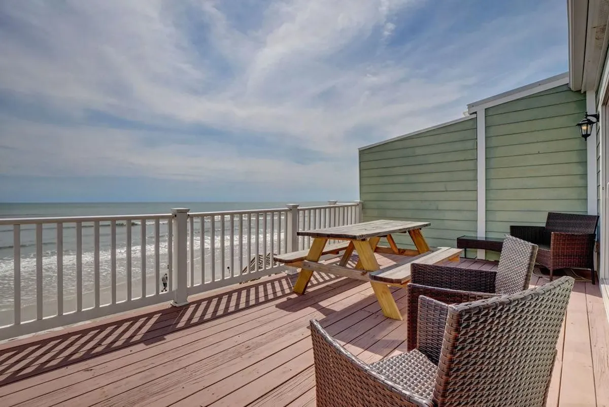 An outdoor space equipped with a picnic table and seating area overlooking the ocean. The view is expansive, inviting al fresco dining, gatherings with friends and family, or simply enjoying the sunset. The calm, inviting setting highlights the versatility of the deck area for all-day enjoyment.