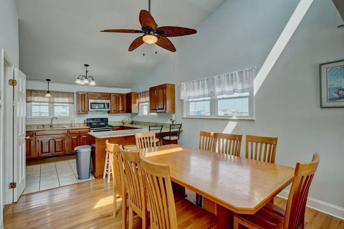 The photo captures a warm, inviting dining area adjacent to a kitchen island, featuring a wooden dining table, comfortable chairs, and ample windows letting in abundant daylight. The space evokes a cozy, communal atmosphere ideal for shared meals and memorable family moments.