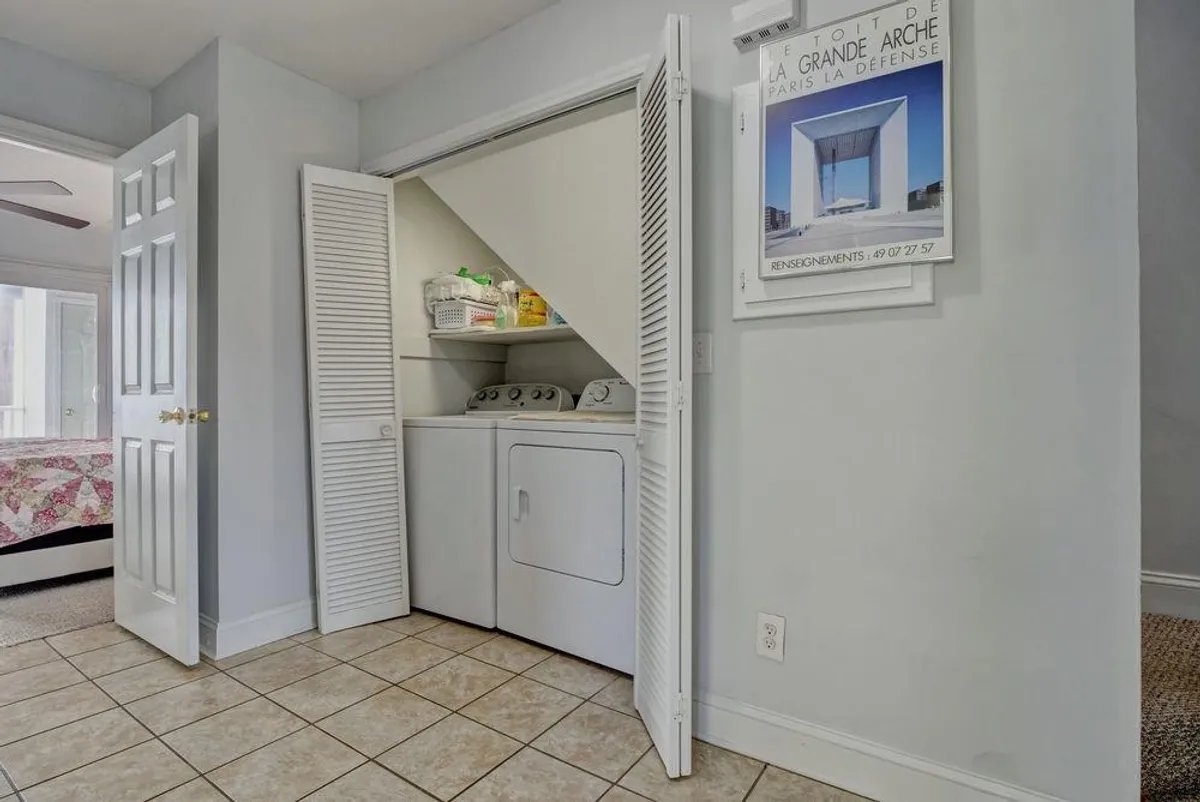 This image features a practical and welcoming laundry area with modern appliances, open closet doors revealing storage space, and decorative wall art that adds a homey touch. The setting is tidy and organized, emphasizing ease of use and self-sufficiency.