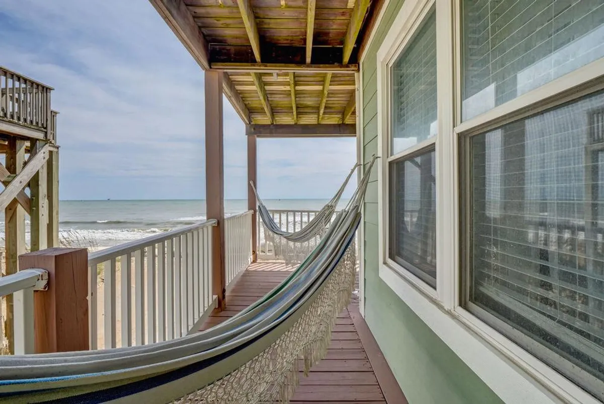 A tranquil wooden deck featuring a hammock perfectly positioned to take in unobstructed views of the ocean. The railing frames the sweeping seascape, while gentle sunlight and ocean breezes set a serene tone. The inviting hammock and open-air aspect let guests imagine relaxing outdoors, hearing the waves and feeling the salty air.