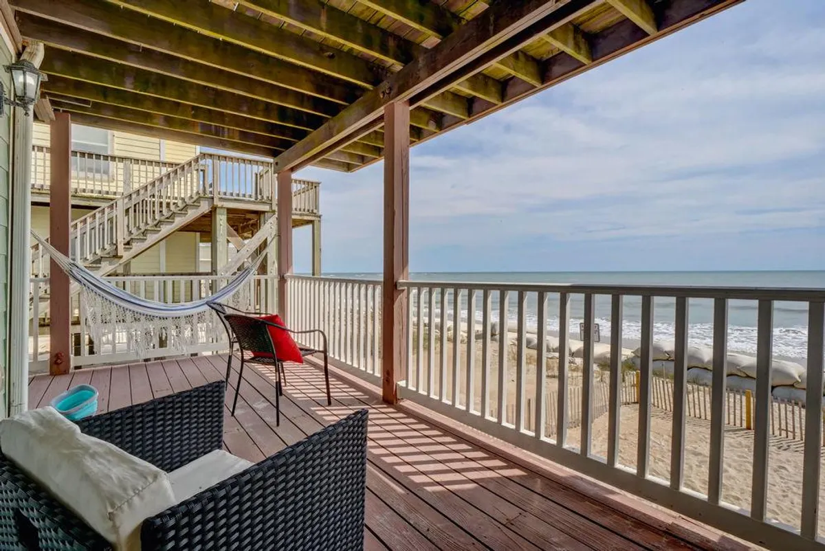 A tranquil outdoor scene featuring a hammock and outdoor seating on a deck overlooking the beach. The area is designed for relaxation and taking in views of the ocean, with railings framing the seascape. It suggests a place to unwind after a day of play, with the sounds and sights of the shore nearby.